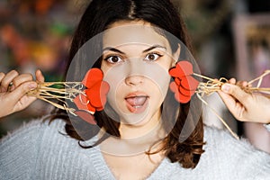 Pretty young brunette girl chooses decor for Valentine`s Day. Girl holding red hearts on a stick, festive decor