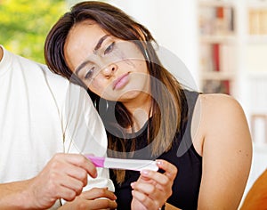 Pretty young brunette woman holding pregnancy home test, crying and leaning head on friends shoulder, bookshelves window