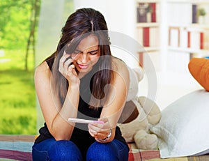 Pretty young brunette woman holding pregnancy home test, touching head with hand and looking depressed, bookshelves