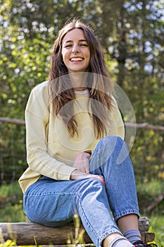 Pretty young brunette woman laughing and looking at camera sitting in a park outdoors on a sunny day.