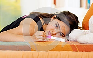 Pretty young brunette woman lying down with pregnancy home test in front, intense emotional stare, garden window