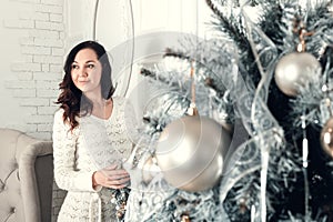 Pretty young brunette woman standing near fir tree in Christmas