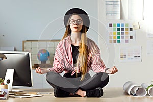 Pretty young business woman doing yoga on the table in the office.