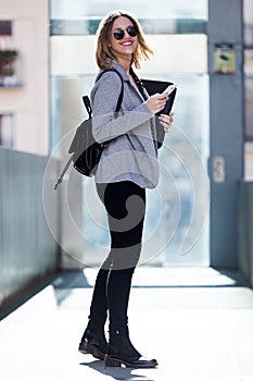 Pretty young business woman looking at camera while using her mobile phone in the street.