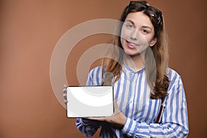 Pretty young business woman in a striped shirt posing on a brown background with a tablet in her hands. Portrait, studio