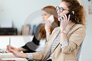 Pretty young business woman using her mobile phone in the office