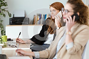 Pretty young business woman using her mobile phone in the office.