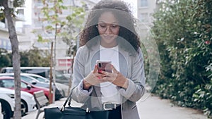 Pretty young business woman using her smart phone while drinking coffee walking down the street.