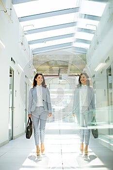 Pretty young business woman walking with briefcase in the office hallway