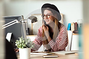 Pretty young business woman working with laptop while using her mobile phone in the office.