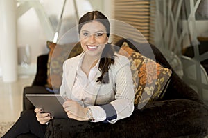 Pretty young businesswoman with digital tablet sitting in office waiting room