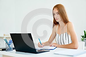 Pretty young businesswoman working on laptop in modern office.