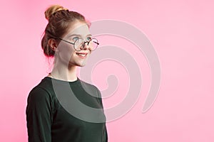 Pretty young casual woman with hair bun looking at camera with smile over pink