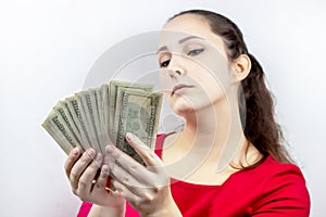 Pretty young caucasian brunette woman in casual red dress holding american dollars in her hands. Finance and money concept