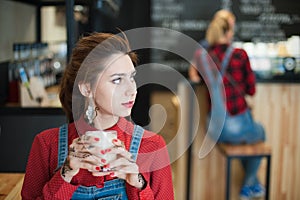 Pretty young caucasian girl in trendy denim costume with glass of white coffee sitting in coffeehouse