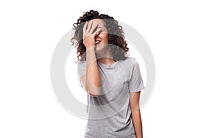 pretty young caucasian woman with black curly hair dressed in a gray t-shirt shy covering her face