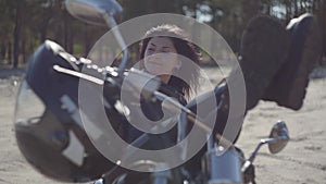 Pretty young caucasian woman in a black leather jacket and pants lying on a motorcycle. Hobby, traveling and active