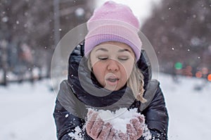 Pretty young Caucasian woman in a cute pink hat on a background of a snowy city alley.