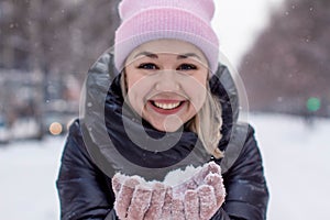 Pretty young Caucasian woman in a cute pink hat on a background of a snowy city alley.