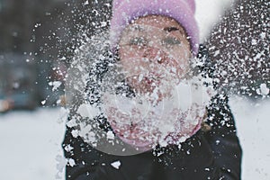 Pretty young Caucasian woman in a cute pink hat on a background of a snowy city alley.