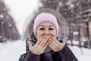 Pretty young Caucasian woman in a cute pink hat on a background of a snowy city alley.