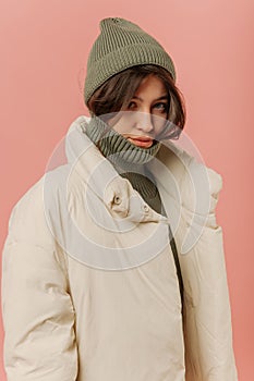 Pretty young caucasian woman with dark hair looks at camera on pink background.