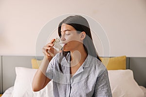 Pretty young caucasian woman drinking water with slice of cucumber sit on bed good morning.