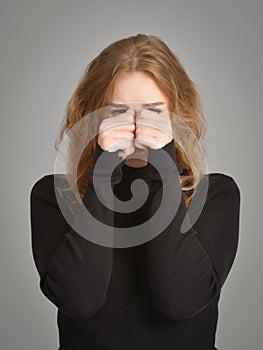 A pretty young Caucasian woman looks furtively, covering her face with her hands