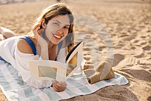 Pretty young caucasian woman spends leisure time reading book lying on beach sunny day.