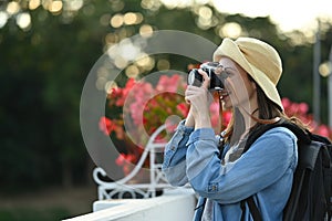 Pretty young caucasian woman traveller with backpack taking photo with digital camera while standing on a bridge over a
