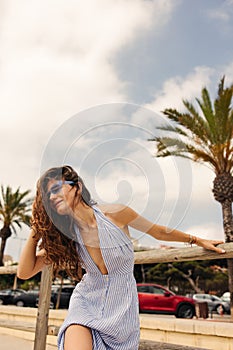 Pretty young caucasian woman with wavy hair posing on camera in cloudy weather.