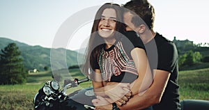 Pretty young couple happy spending a lovely time together in the middle of nature sitting on their motorcycle