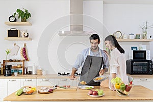 Pretty young couple in the kitchen, family of two preparing food, woman sitting on kitchen table and helping man