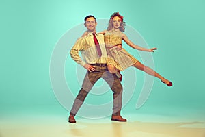 Pretty young couple in retro 80s, 90s fashion style outfit dancing against gradient mint background. Look happy, excited