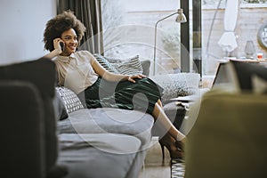 Young curly hair african woman relaxing at home and using mobile phone