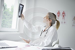 Pretty young doctor looking at x-rays in her doctor`s office