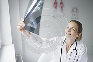 Pretty young doctor looking at x-rays in her doctor`s office