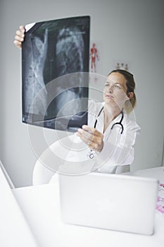 Pretty young doctor looking at x-rays in her doctor`s office