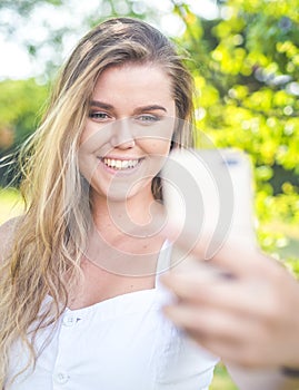 Pretty young female with big smile are taking selfie oudoor.