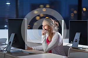 Pretty, young female college student using a desktop computer/pc in a college library - burning the midnight oil, working hard to