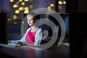 Pretty, young female college student using a desktop computer/pc in a college library - burning the midnight oil, working hard to