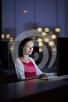 Pretty, young female college student using a desktop computer/pc in a college library - burning the midnight oil, working hard to