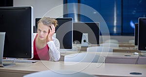 Pretty, young female college student using a desktop computer/pc in a college library (shallow DOF; color toned image)