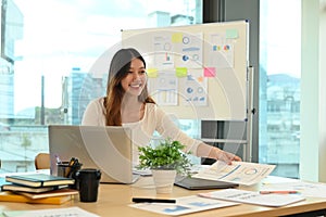 Pretty young female employee using laptop and working with financial reports at modern office