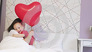 pretty young female mother baby toddler kid white bed red heart balloons holiday