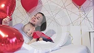 pretty young female mother baby toddler kid white bed red heart balloons holiday