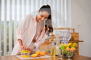 Pretty young female using her hands to squeeze juice from fresh orange fruit in the kitchen room at home