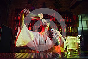 Pretty young girl, bartender working in bar, making delicious cocktails. Woman putting ice cubes in shaker, preparing