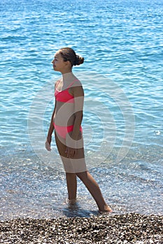 Pretty young girl in bikini standing on the beach near by sea