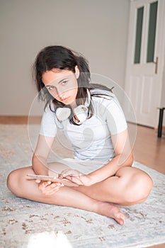 Pretty young girl on the carpet at home with a smartphone in her hand and headphones around her neck. Apartment living. Home life